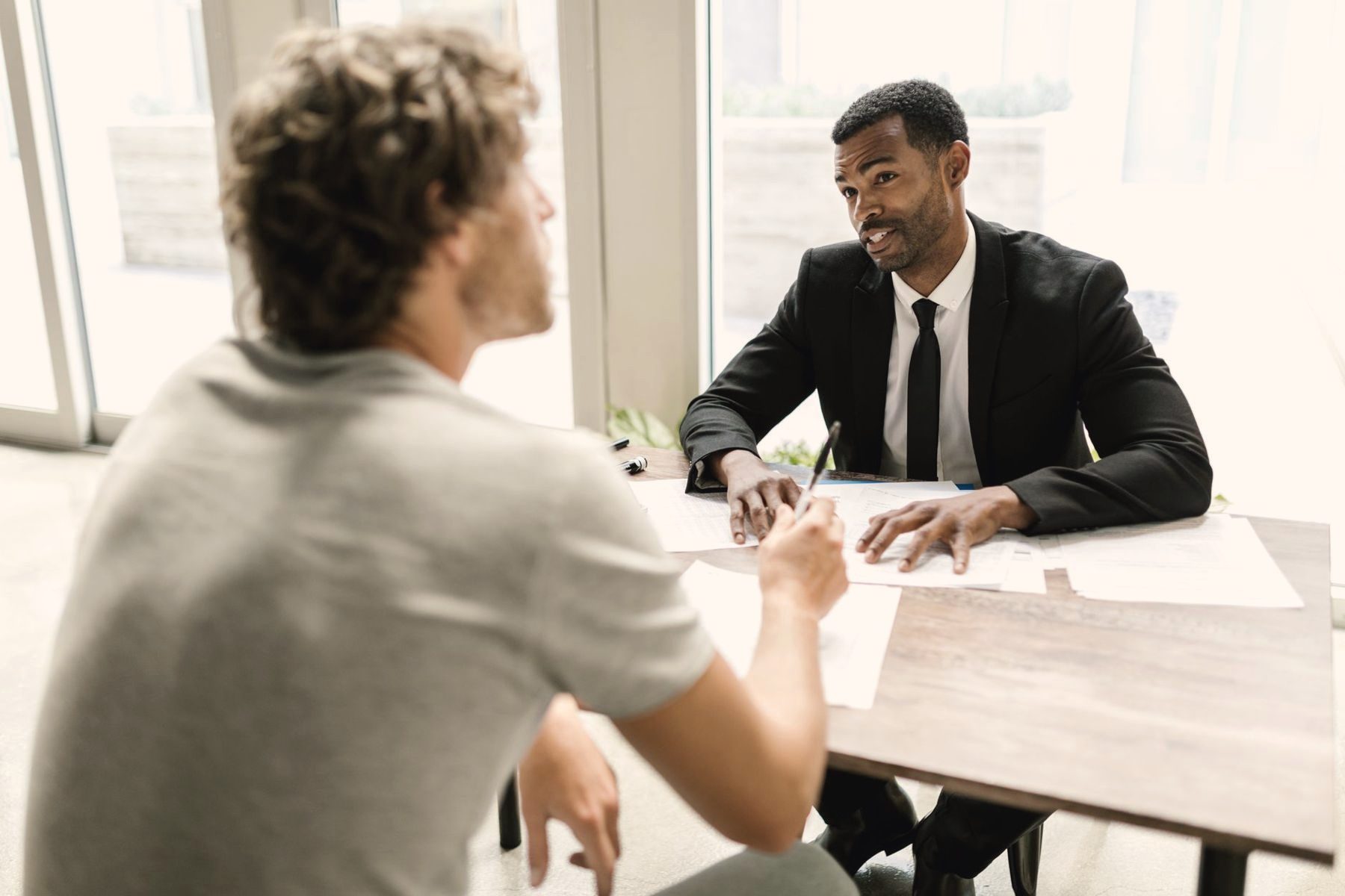 An advisor in a dark suit reviewing paperwork with a client at a bright office desk